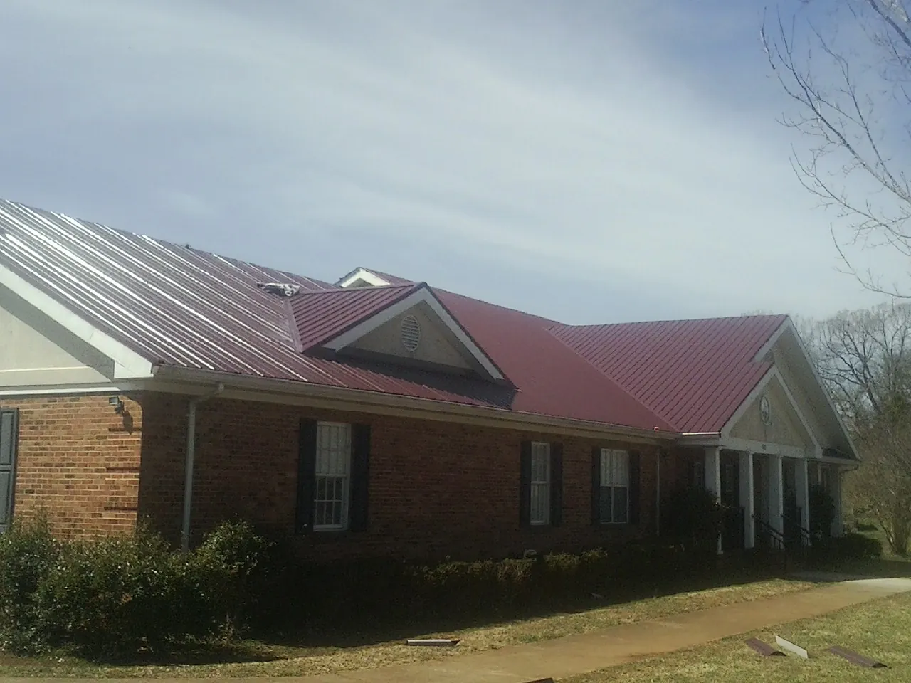 Red metal roof with gabled entries on a long brick building, from a Hail Damage Roof Repair job in Deming