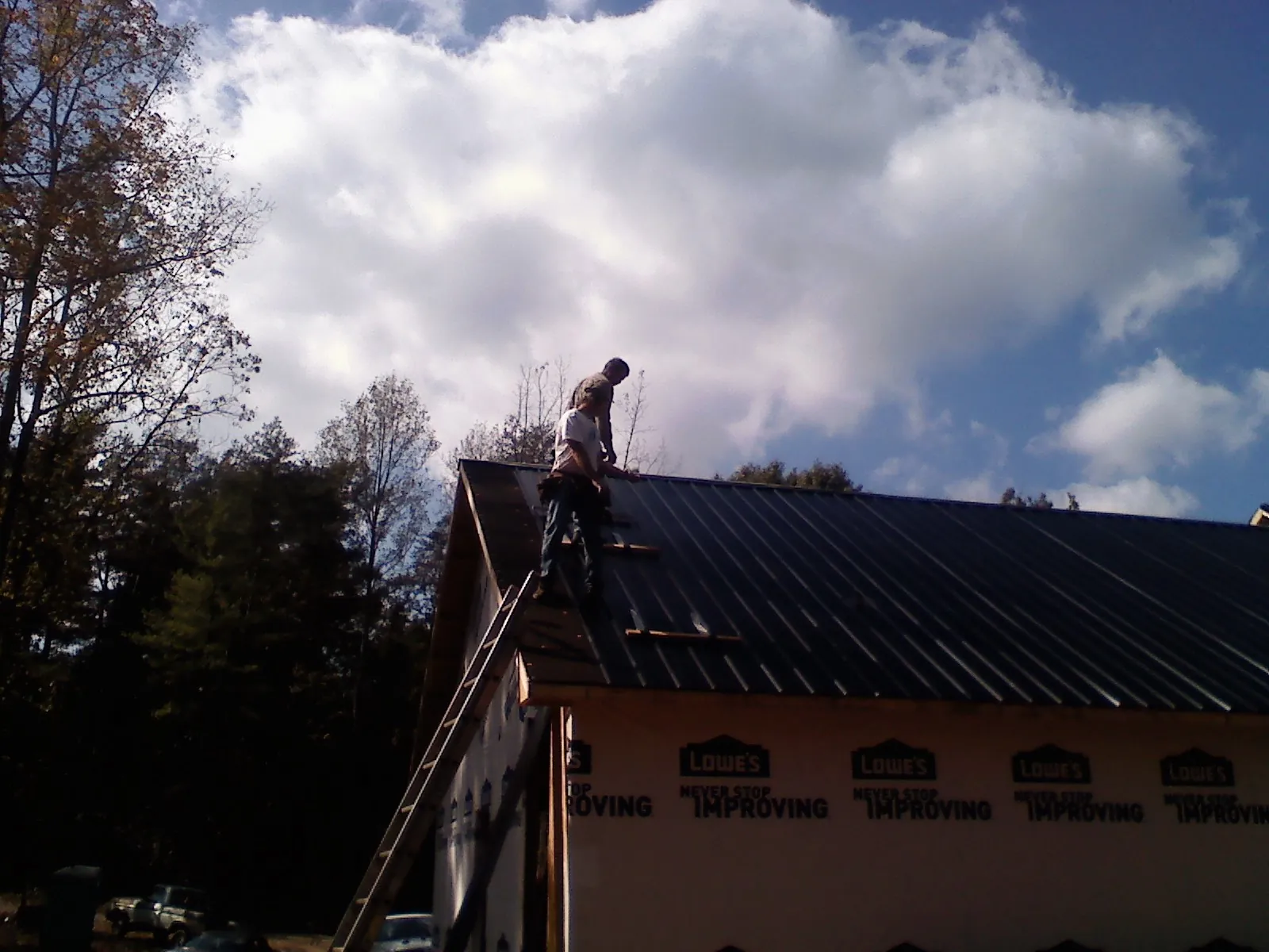 Roofer fastening dark metal panels high against a cloudy sky, from a Roof Inspection job in Deming