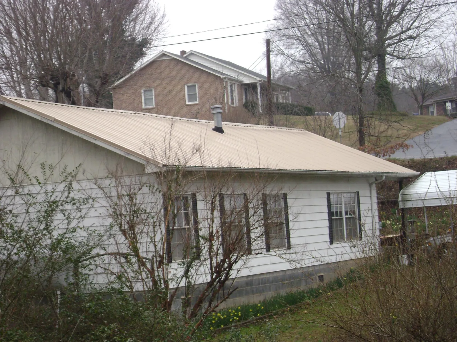 Tan metal roof on a white sided house set into a hillside — Commercial Roofing by Roofing Brothers in Deming